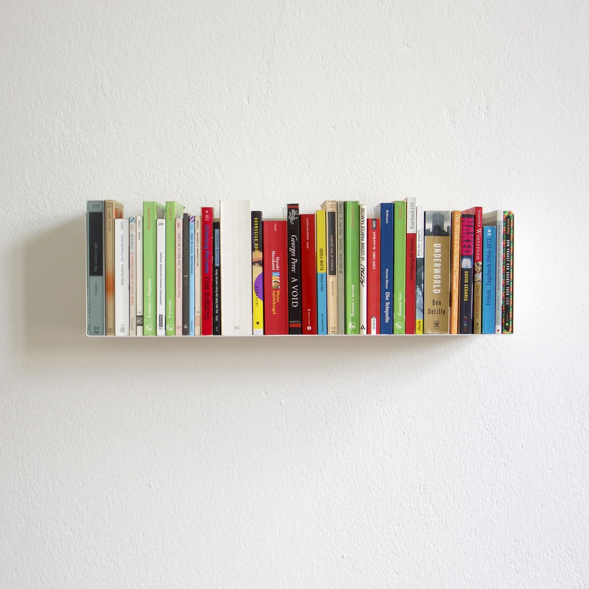 Weißes Wandregal von Müller Möbelwerkstätten, Modell a Linea1, voll mit bunten Taschenbüchern vor einer weißen Wand.