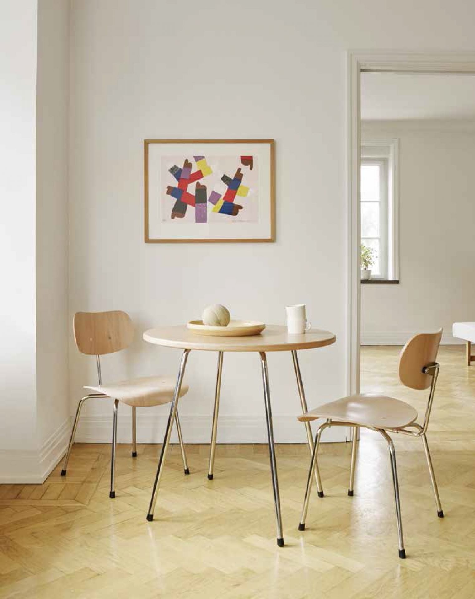 Zwei Wilde+Spieth SE 68 Stühle aus Holz und Stahl an kleinem Esstisch in hellem Raum.