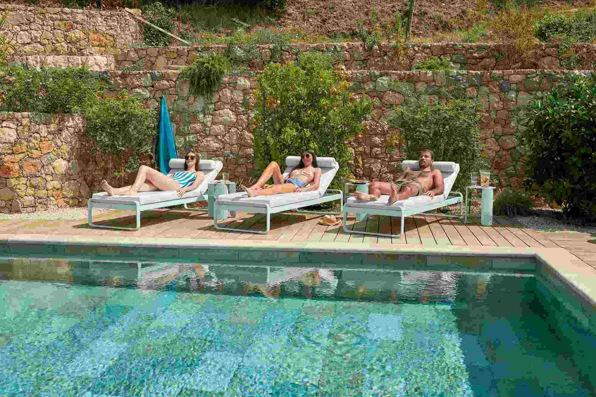 Drei Personen entspannen auf modernen Bellevie Sonnenliegen am Pool; Outdoor-Möbel für Garten und Terrasse.