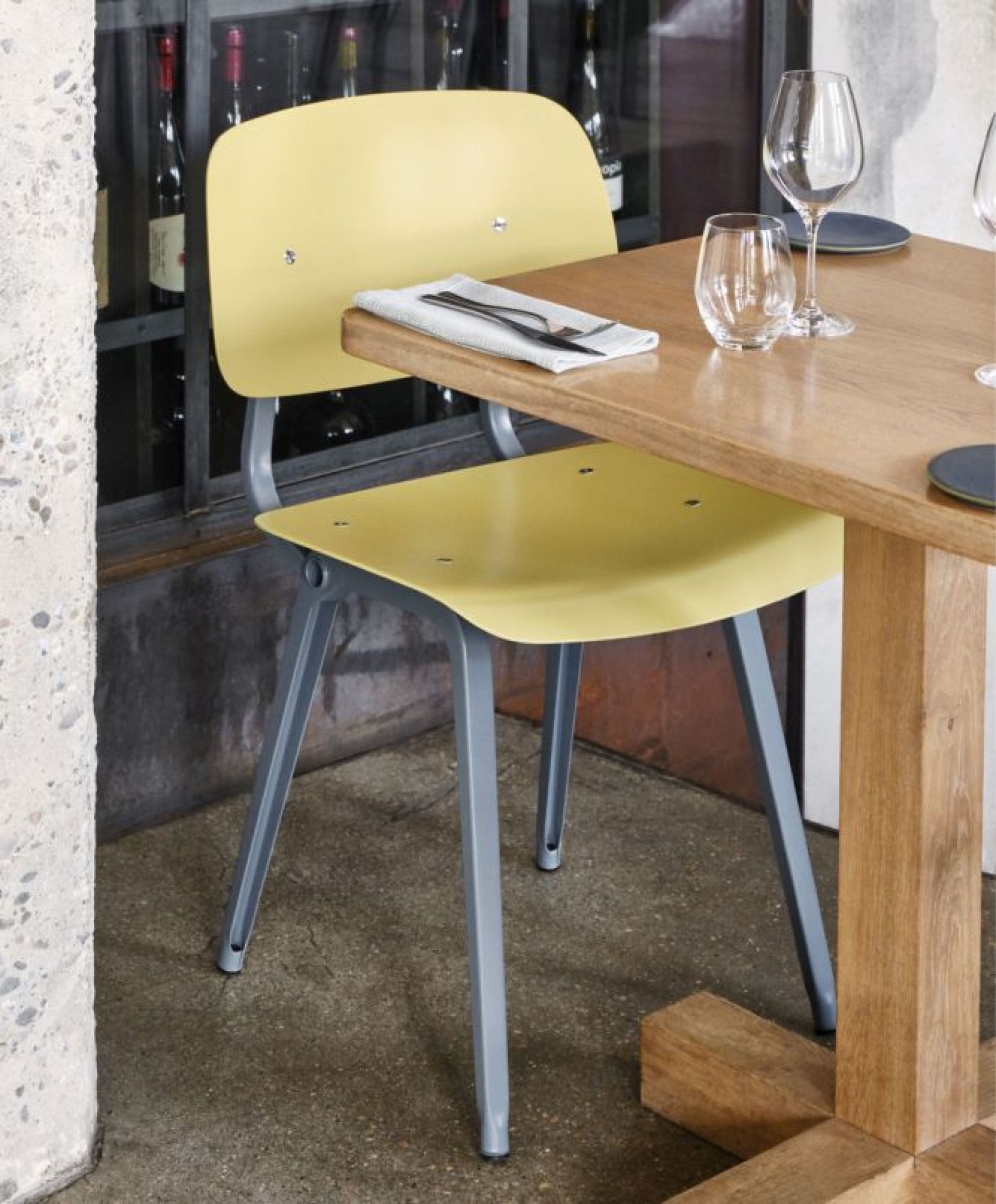 Gelber Hay Revolt Chair Stuhl mit grauem Metallgestell am Esstisch im Restaurant.