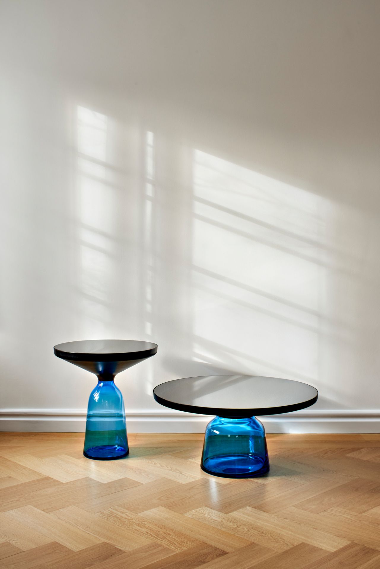 Zwei blaue Bell Coffee Table Couchtische von ClassiCon auf einem hellen Parkettboden vor einer weißen Wand.