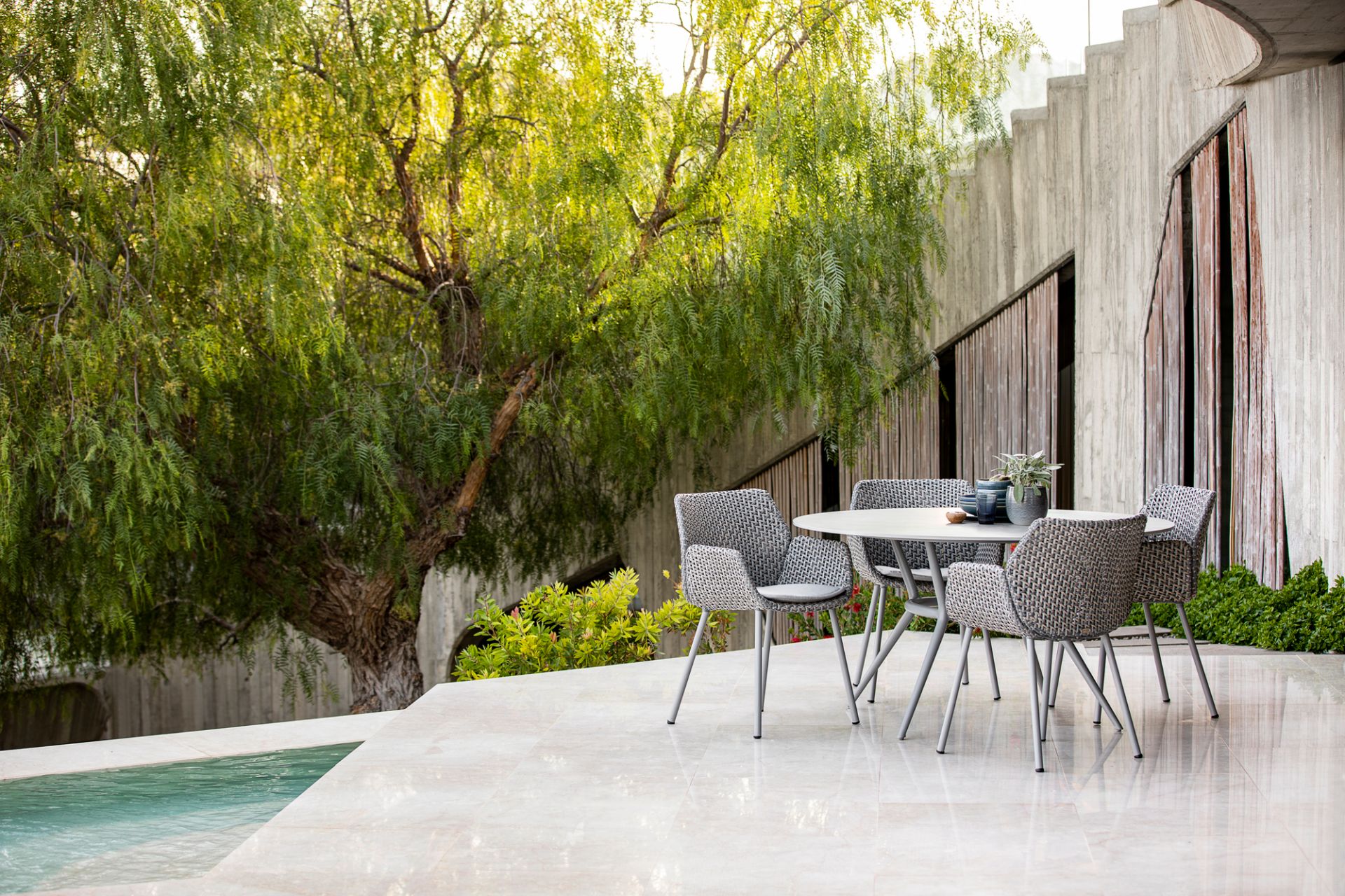 Cane-Line Vibe Sessel: Elegante Outdoor-Sitzgruppe mit Flechtstruktur und modernem Design auf einer Terrasse am Pool.