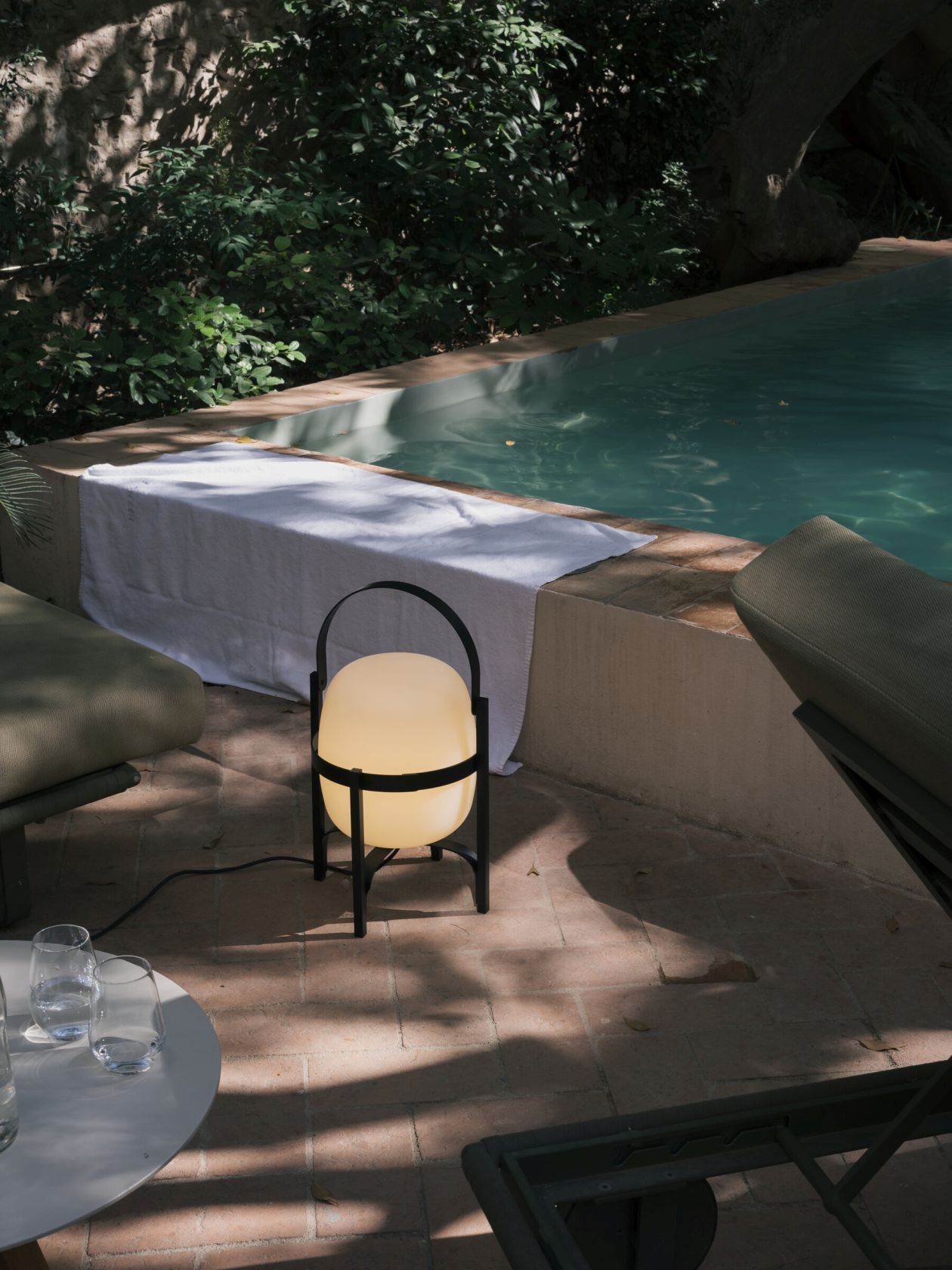 Cesta Outdoor Tischleuchte von Santa & Cole in Schwarz neben Pool und Liegestuhl.