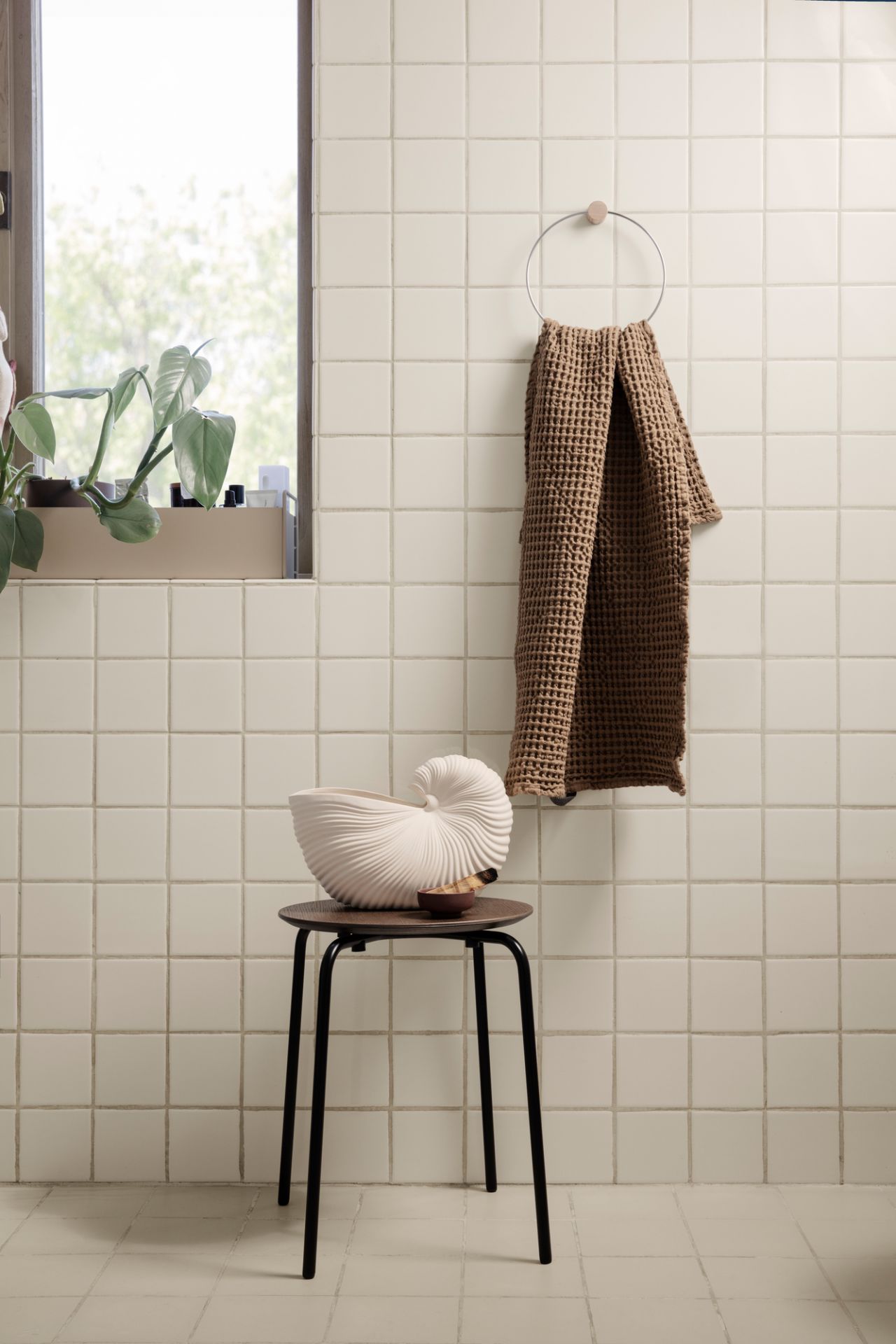Helle Badezimmer-Szene mit Ferm Living Shell Pot Vase auf Hocker, Handtuch an der Wand.