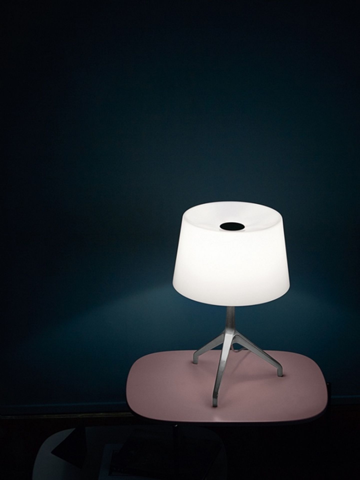 Weiße Lumiere Tischleuchte von Foscarini auf einem rosa Tisch vor dunkler Wand.