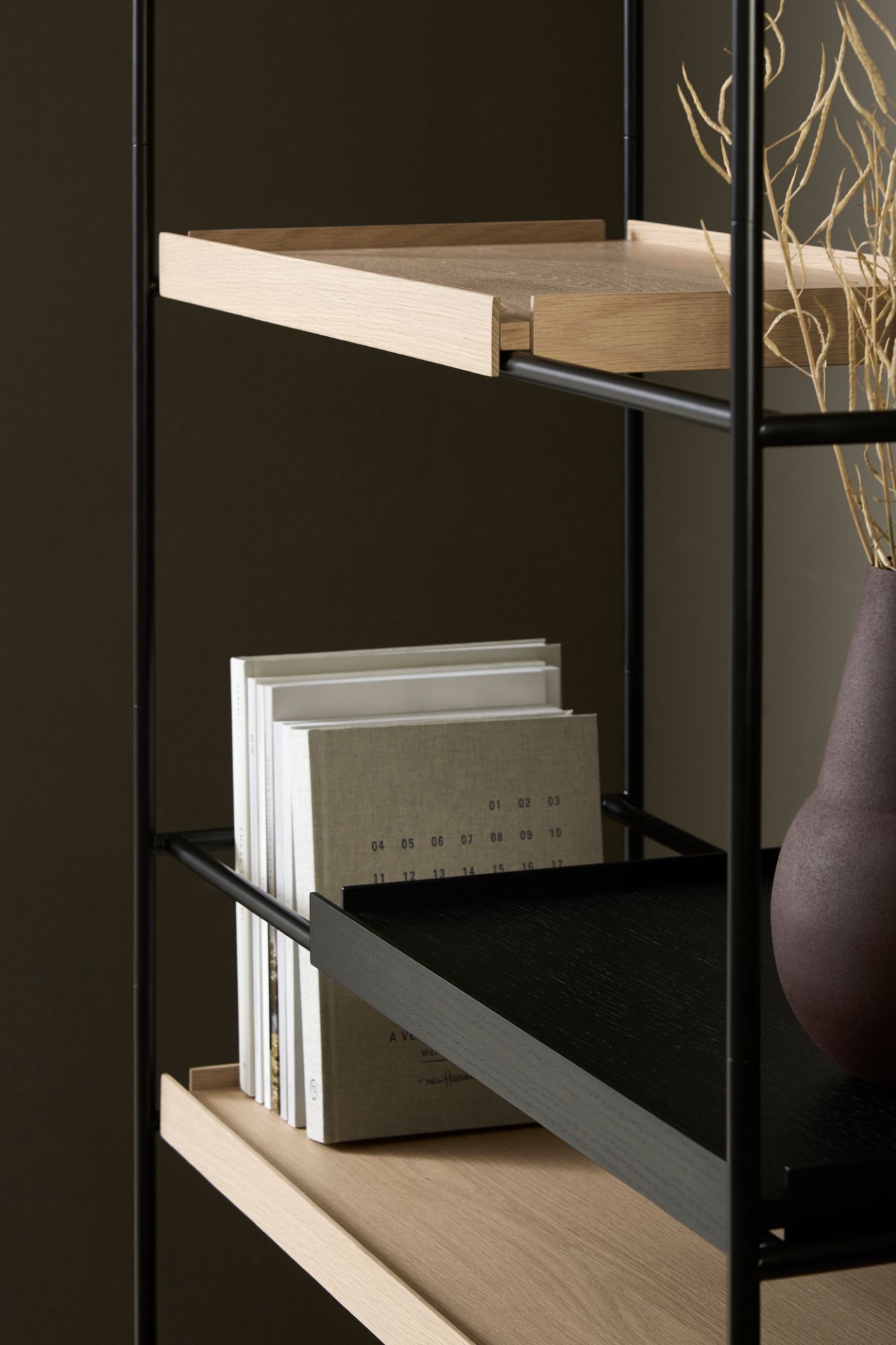 Detailaufnahme des hohen Tray Regals von Woud, Eiche natur und schwarz, mit Büchern und Dekoration.