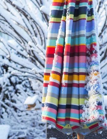 Weishäupl Klassiker Schirm: Detailaufnahme eines geschlossenen, farbenfrohen Sonnenschirms im Winter, teilweise mit Schnee bedeckt.