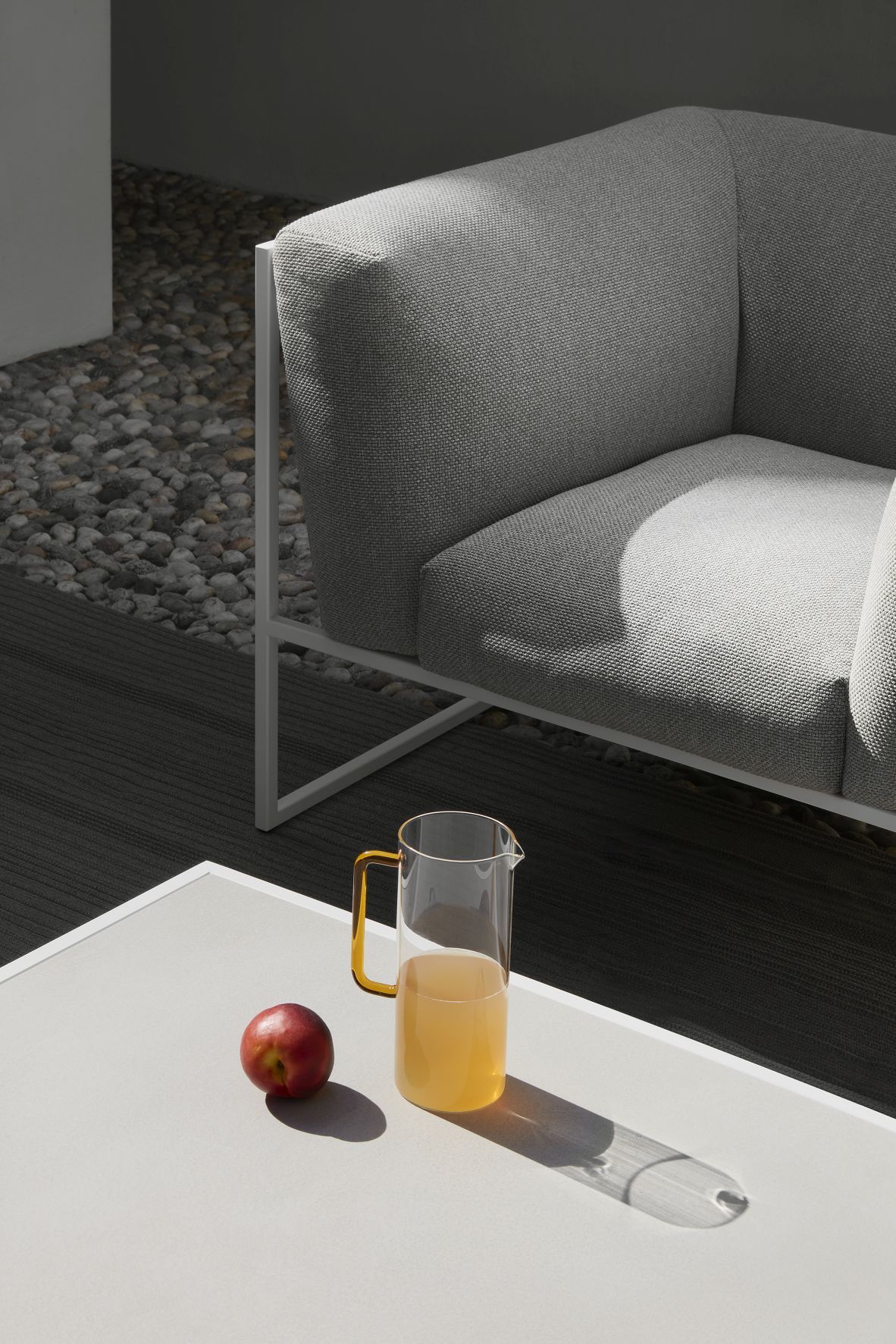 Detailaufnahme des grauen Arpa Outdoor Sofas von MDF Italia mit Tisch, Getränkekrug und Apfel.