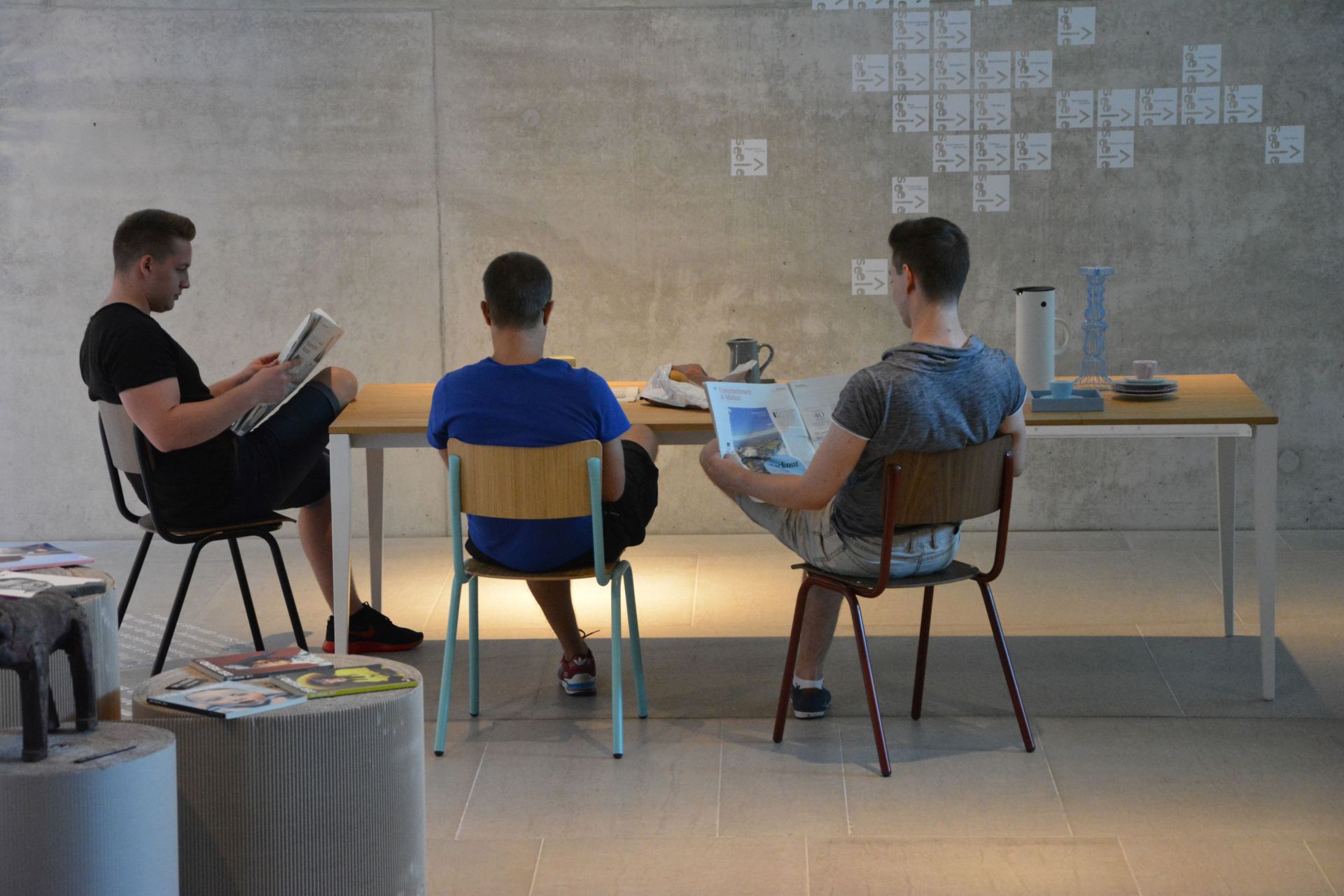 Drei Personen sitzen am Jan Kurtz Jupiter Ausziehtisch und lesen Zeitungen, minimalistisches Design.