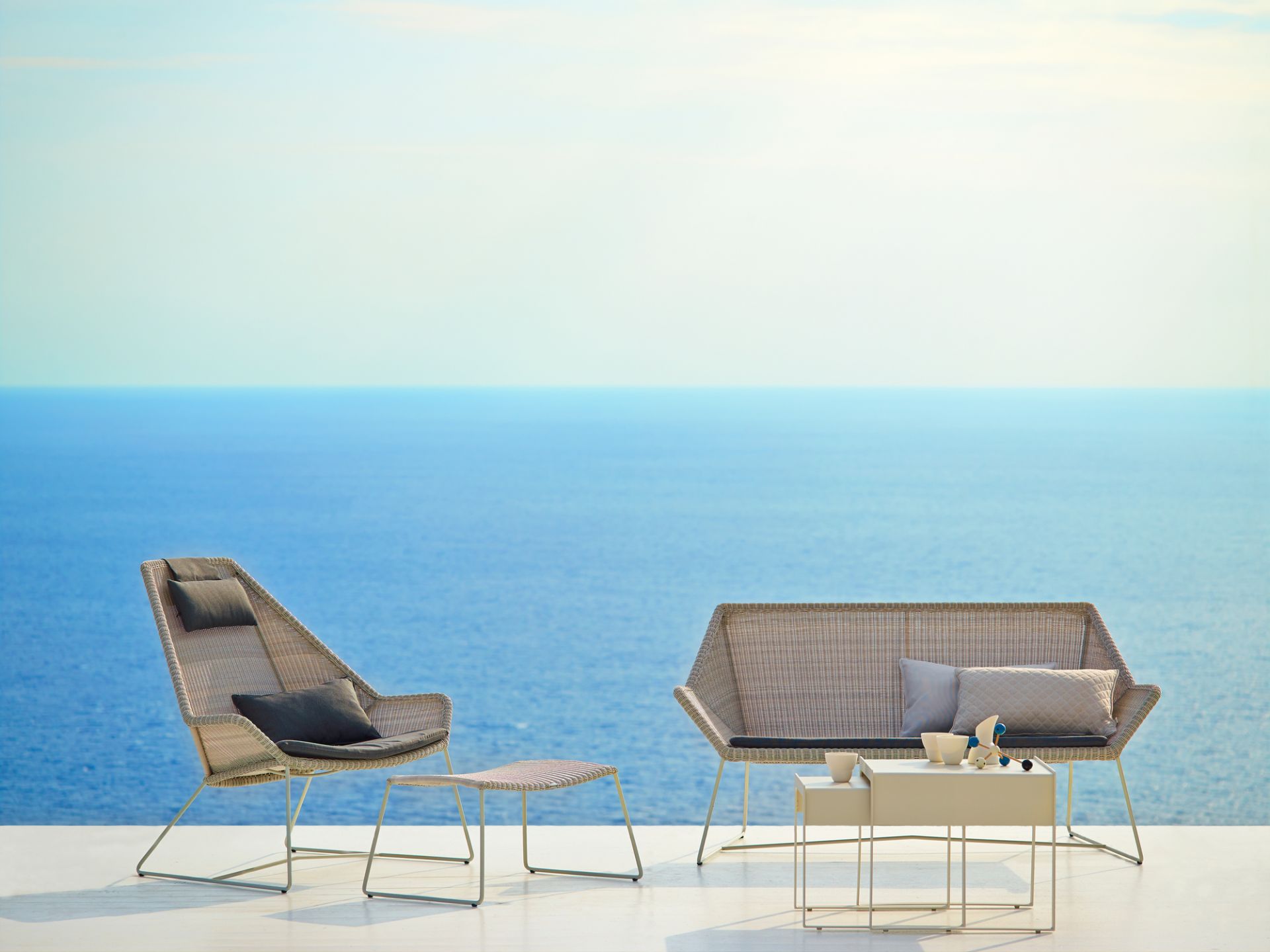 Cane-Line Breeze Outdoor Hocker in Schwarz, Teil eines Loungesets mit Meerblick.