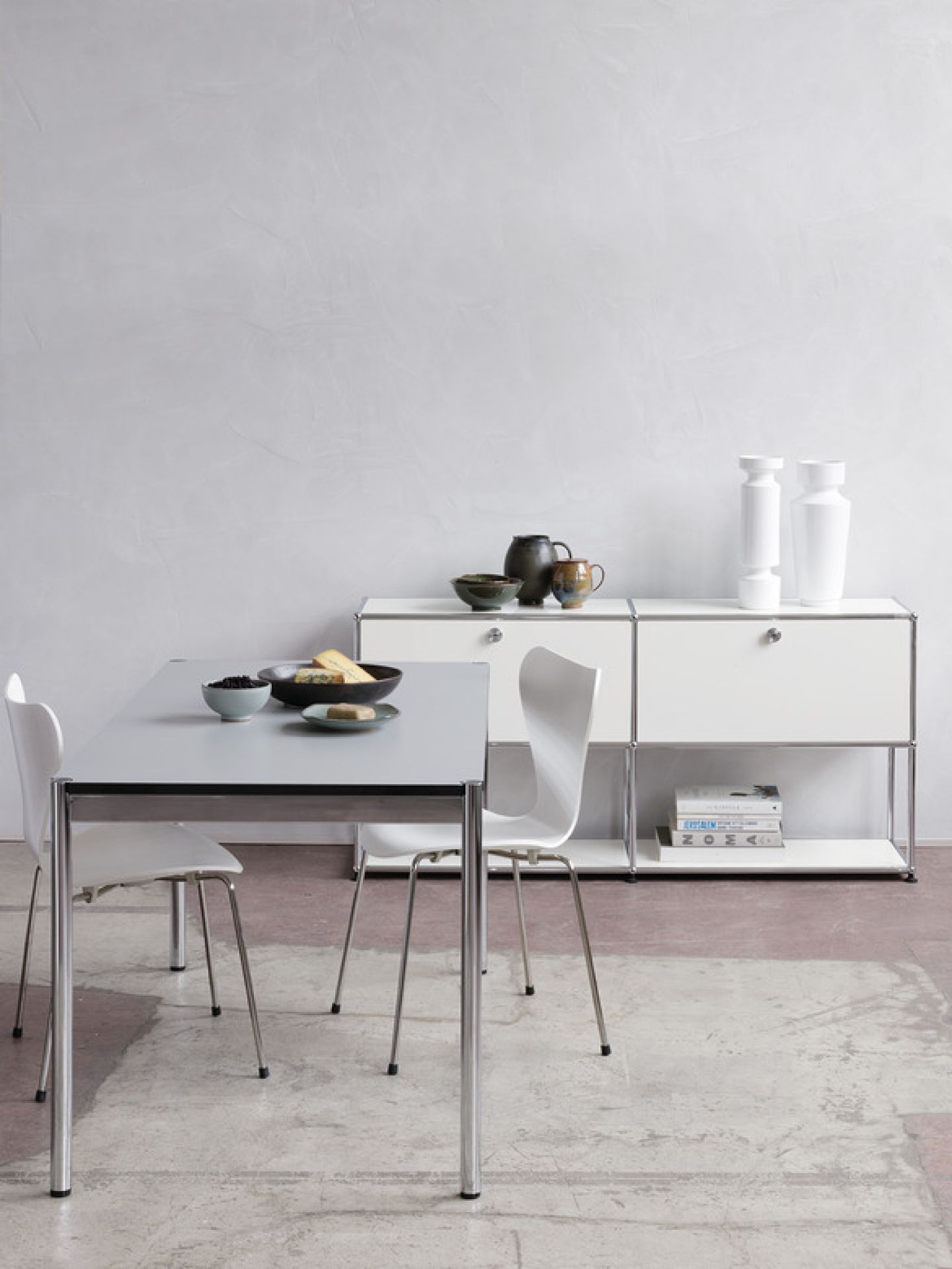 USM Haller Tisch 150x75 cm in Hellgrau mit Chromgestell und passendem weißen Sideboard im Hintergrund.