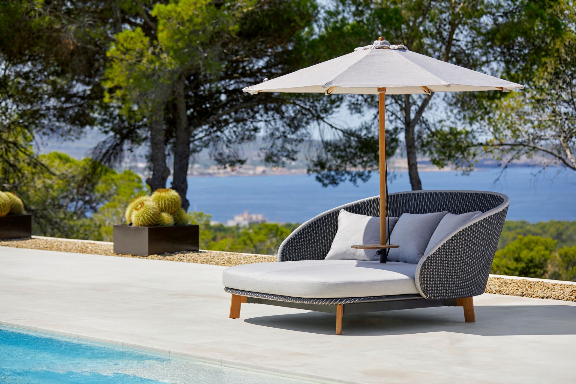 Cane-Line Sonnenschirm für Peacock Daybed neben Pool mit Meerblick im Hintergrund. Outdoor-Sonnenschutz für Gartenmöbel.