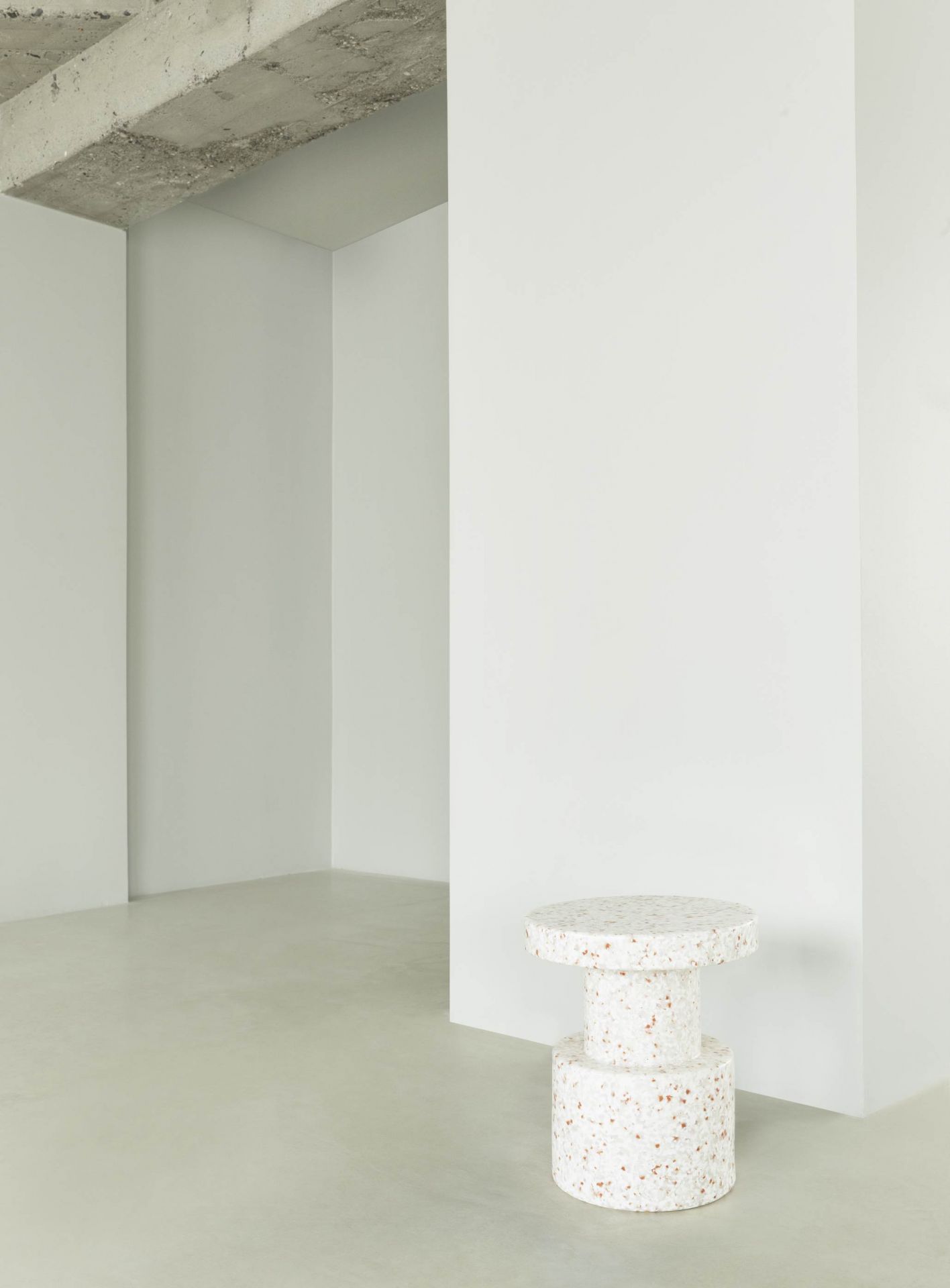 Normann Copenhagen Bit Stool Hocker in Weiß mit Terrazzo-Muster vor minimalistischem Hintergrund.
