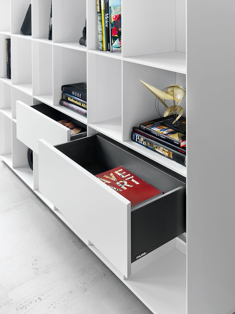 Detailaufnahme des weißen Nex Pur Regals von Piure mit offenen Schubladen und dekorativen Büchern.