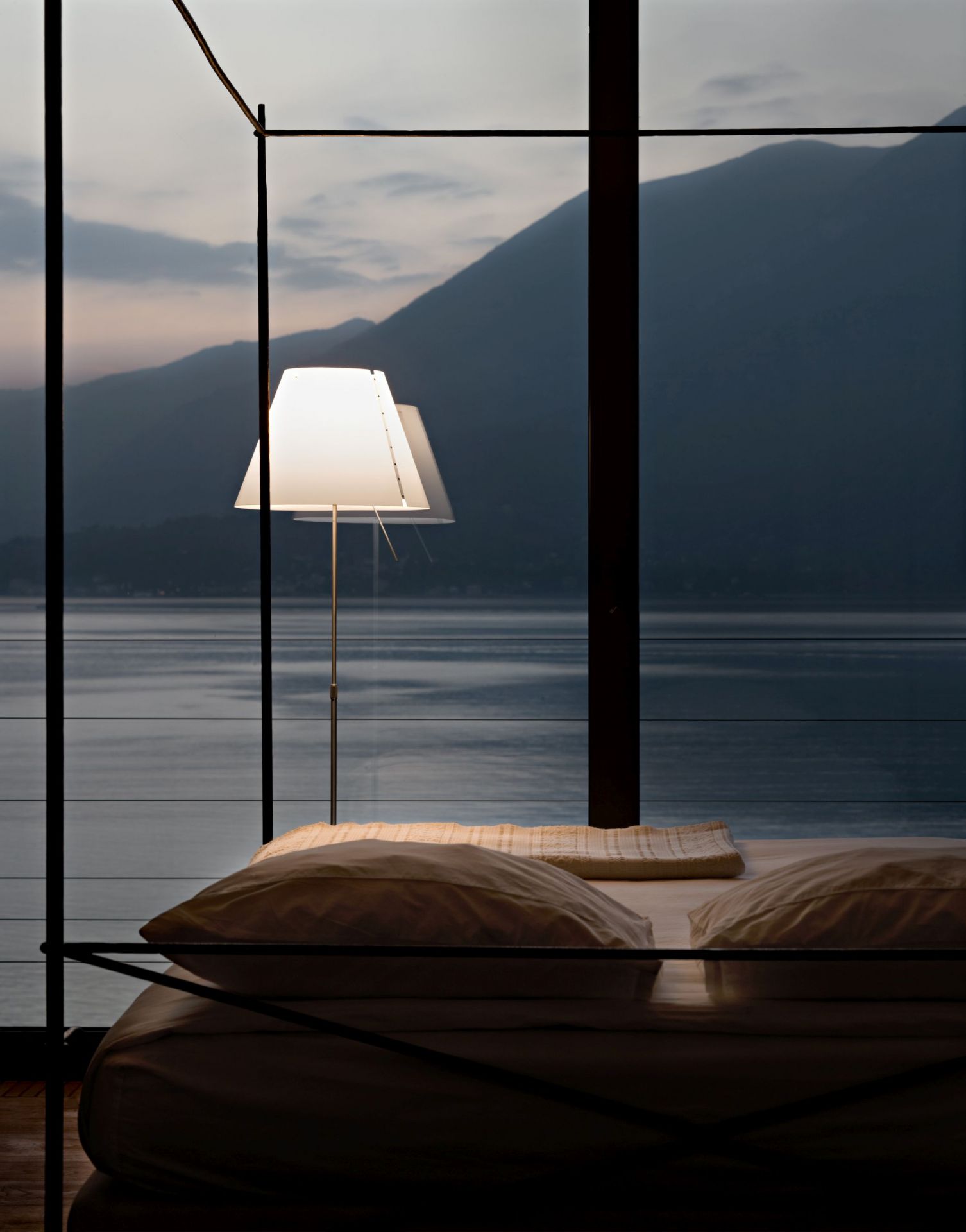 D13 Costanza Tischleuchte von Luceplan neben einem Bett mit Seeblick.