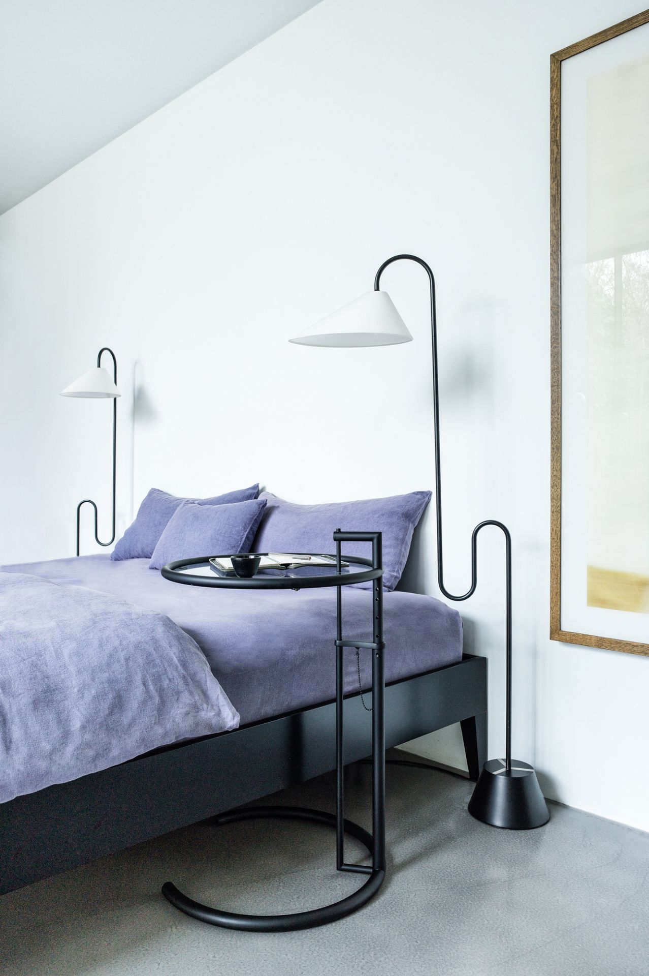 Nahaufnahme des ClassiCon Adjustable Table E1027 Beistelltisches in Schwarz neben einem Bett mit lila Bettwäsche.