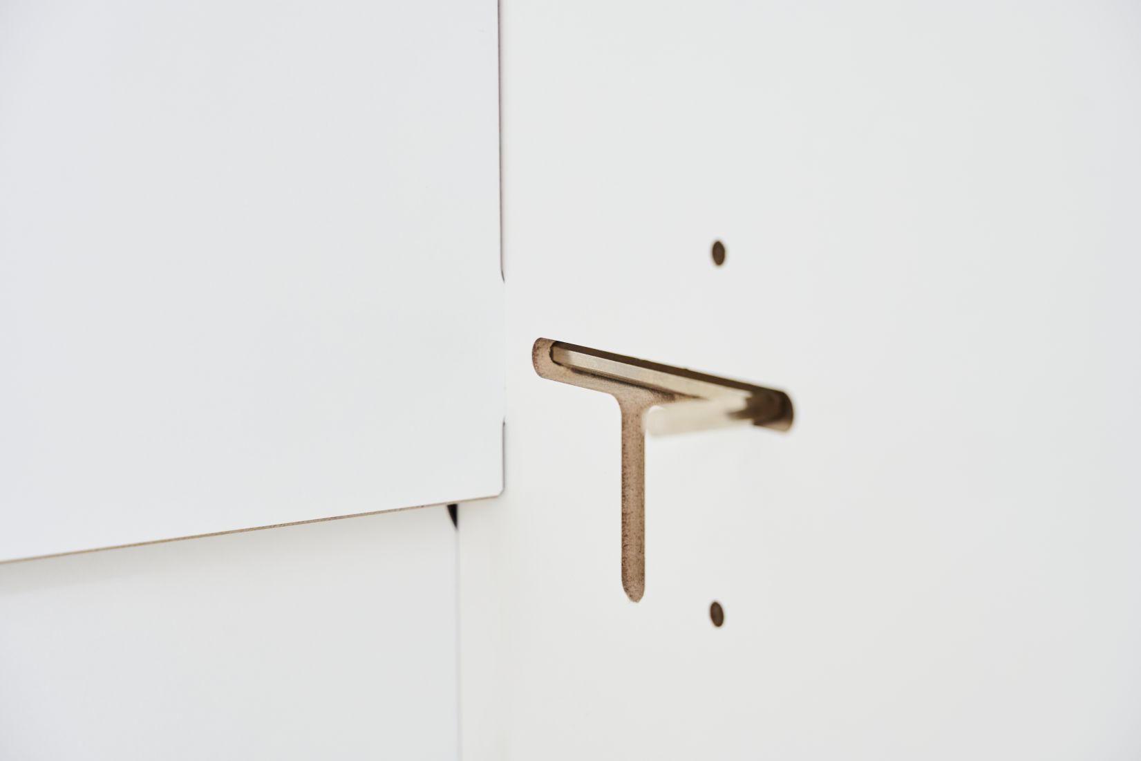 Detailaufnahme Tojo Schrank Grundmodul: Verbindungselement aus Metall in T-Form, weiße Schrankwand.
