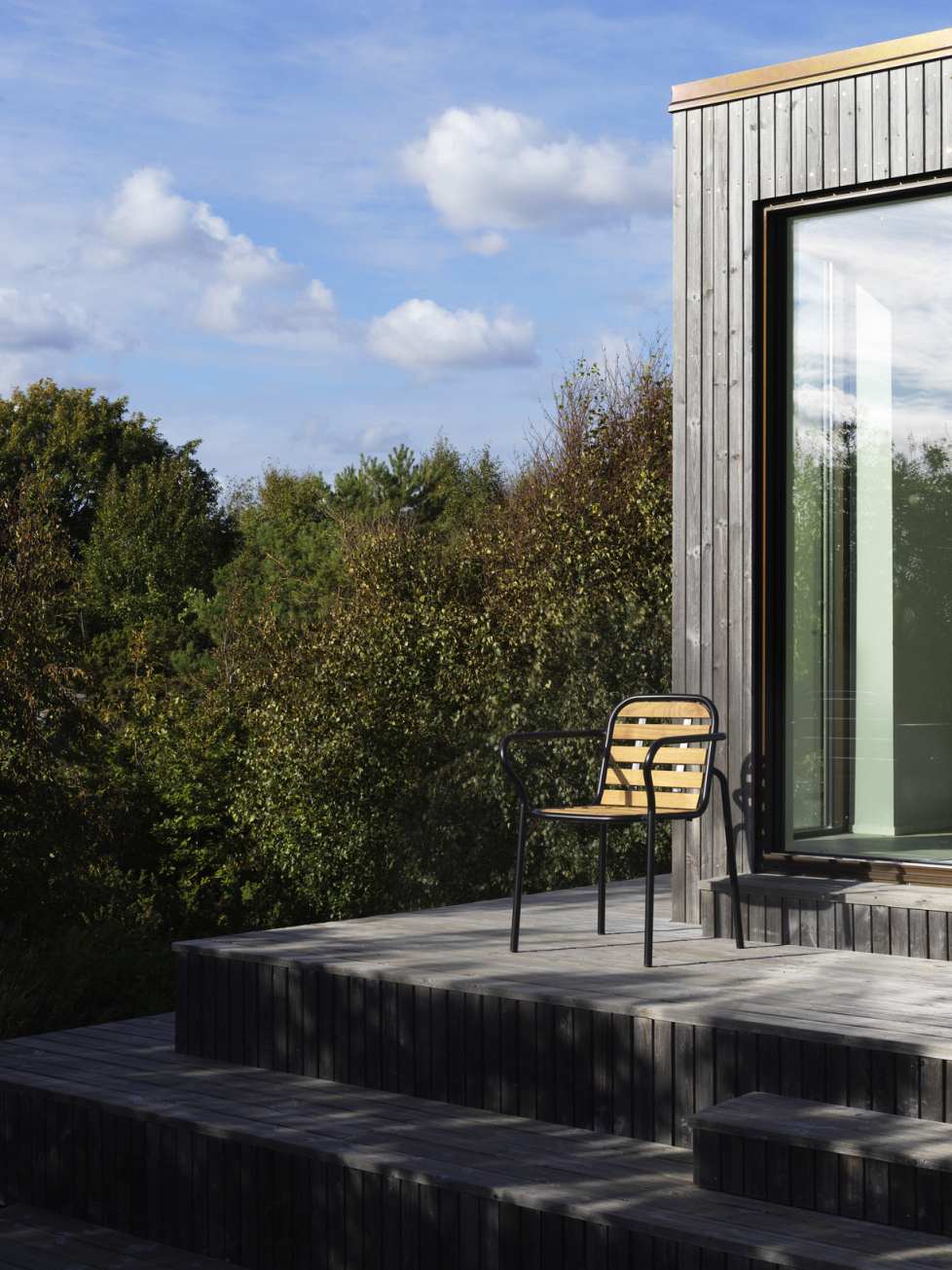 Vig Armchair Armlehnstuhl von Normann Copenhagen auf Holzterrasse vor modernem Haus und Bäumen.