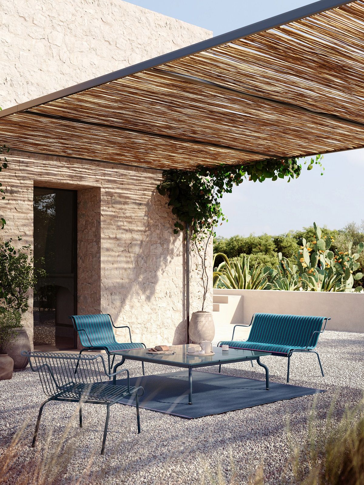 Magis South Outdoor Carpet Teppich in blau unter einer Pergola mit Gartenmöbeln auf Kiesboden.