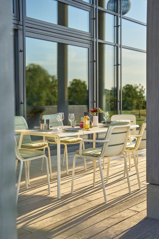Weishäupl Vapio Stuhl Outdoor: Gartentisch mit Stühlen aus Metall und grünen Polsterkissen auf einer Terrasse.
