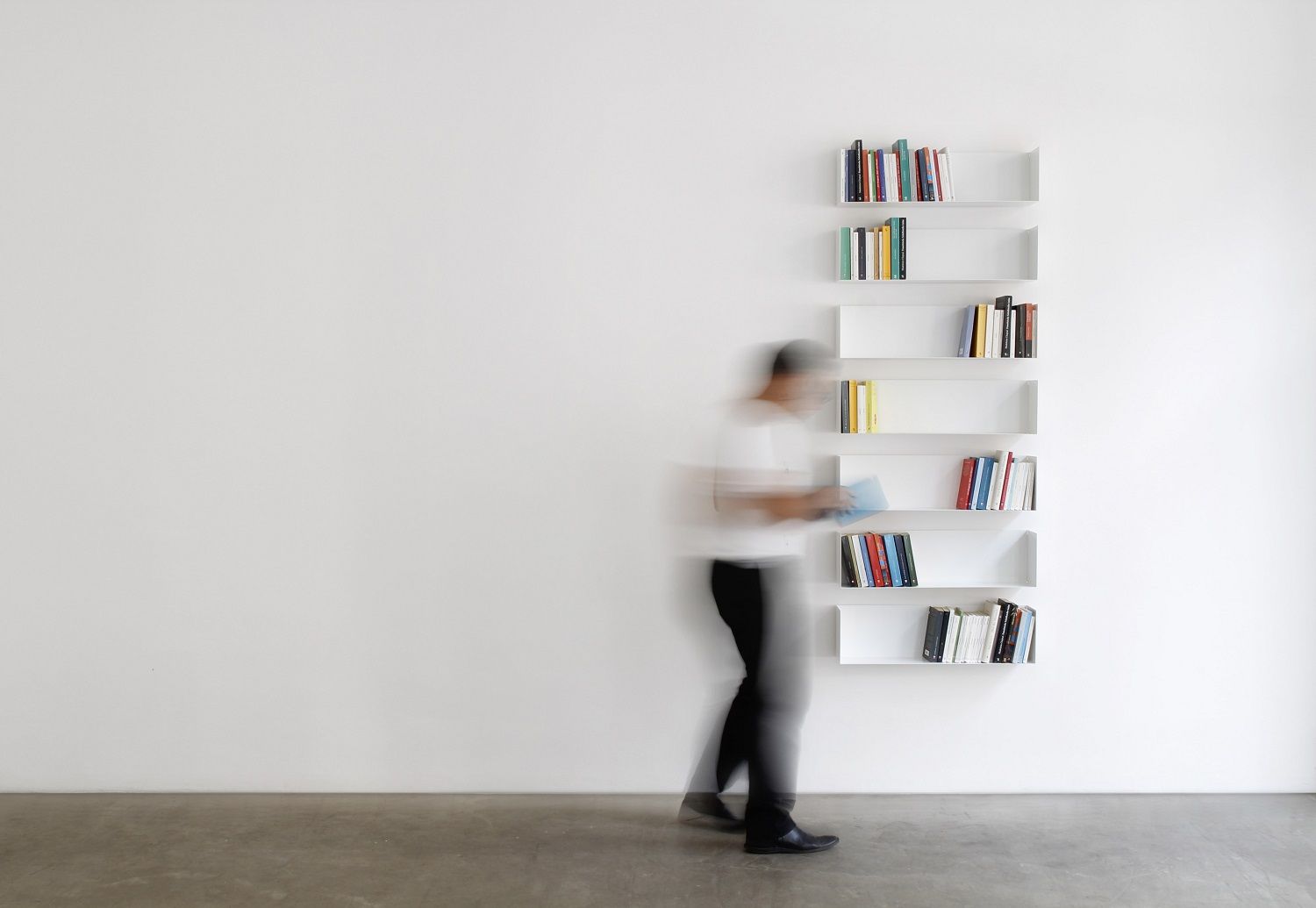 Weißes Taschenbuchregal a Linea1 von Müller Möbelwerkstätten an einer Wand mit Büchern und Person.