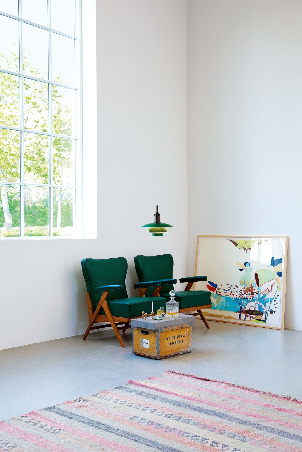 Moderne grüne PH Louis Poulsen Hängeleuchte über zwei grünen Sesseln in einem hellen Wohnzimmer.