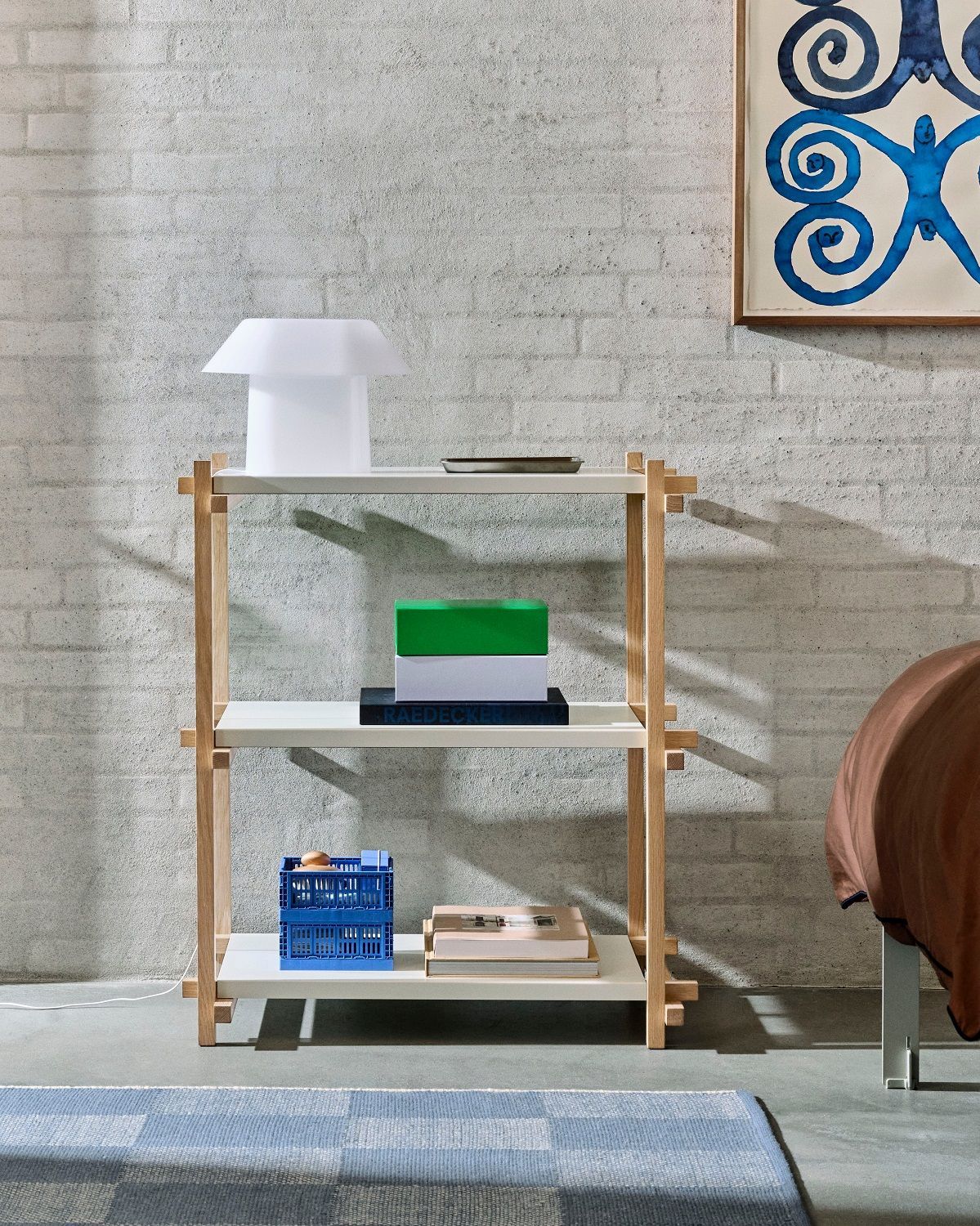 Helles Hay Woody Column Low Regal mit drei Ablageflächen, dekoriert mit Lampe, Büchern und Kiste.