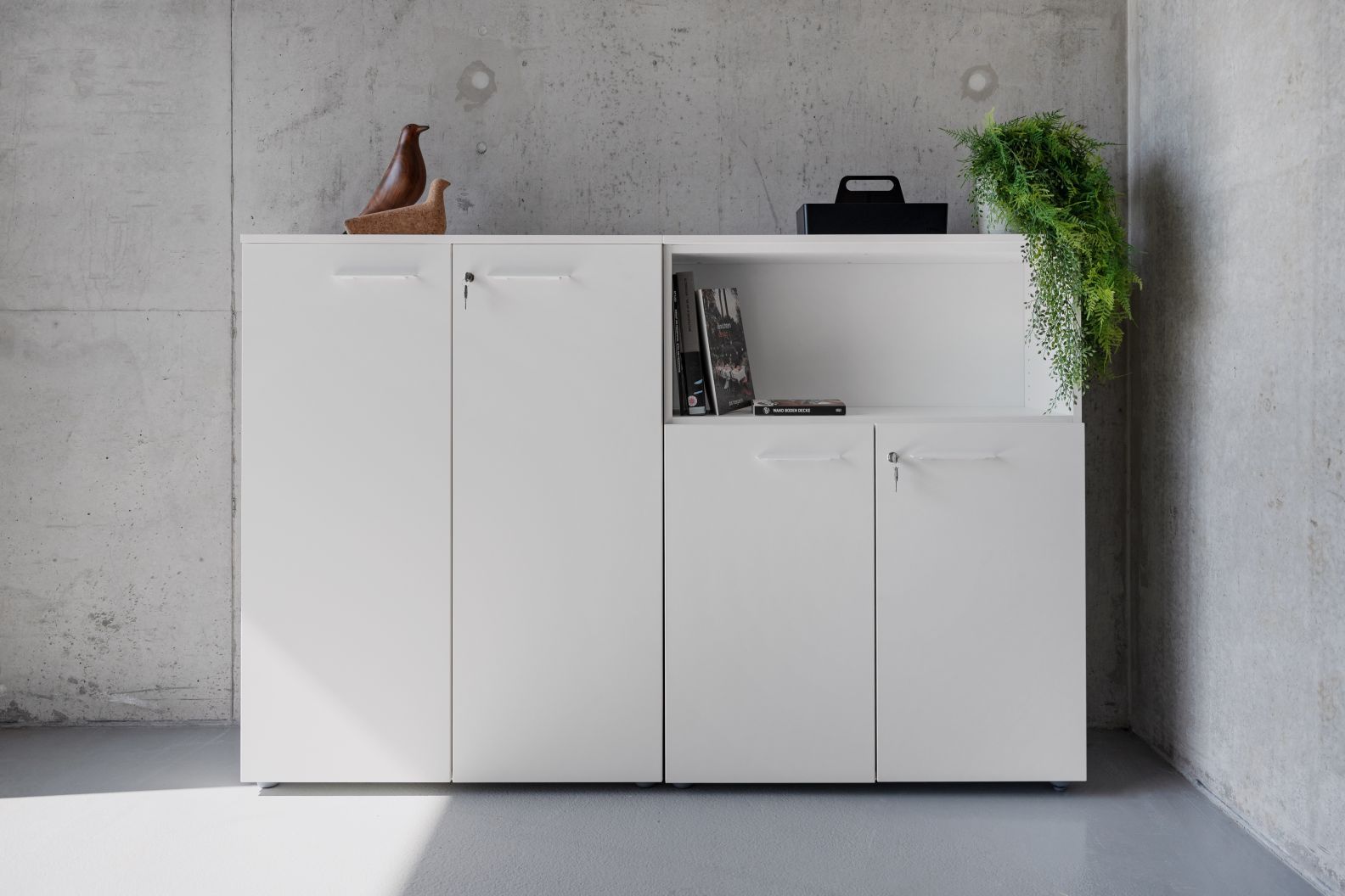 Weißes Sideboard mit Drehtüren, teilweise offen, mit Dekoration. Frezza Passepartout Schrank für Büro und Wohnraum.