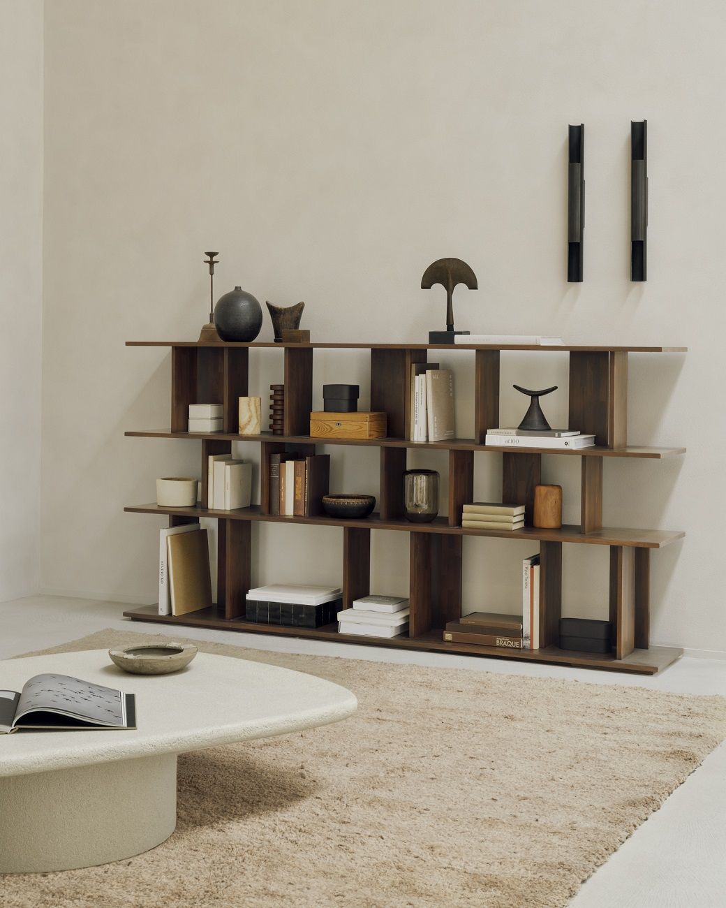 Ethnicraft Elements Couchtisch in Kieselform aus Microcement vor Bücherregal und Teppich.