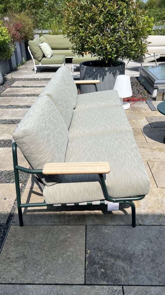 Muuto Settle Lounge Outdoor Sofa mit grünen Rahmen und hellgrauen Polstern auf einer Terrasse.