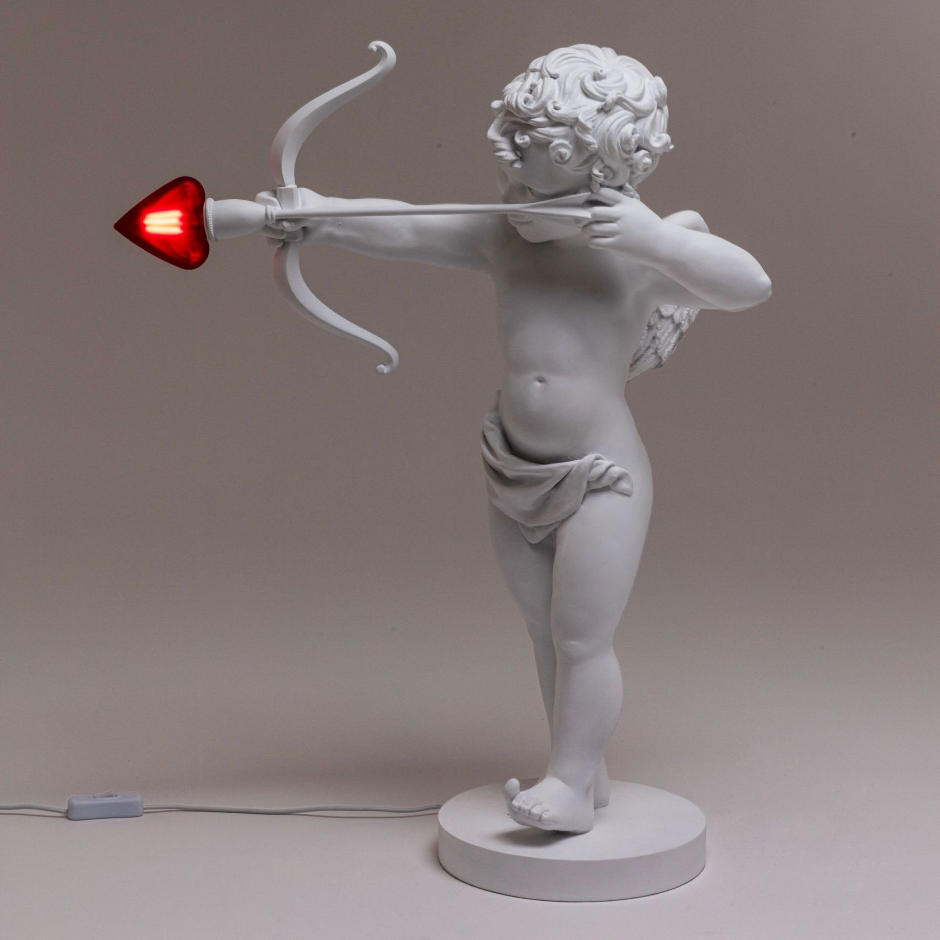 Weiße Amor-Statue als Tischleuchte mit herzförmigem, rotem Pfeil, moderne und romantische Dekoration für Schlafzimmer.
