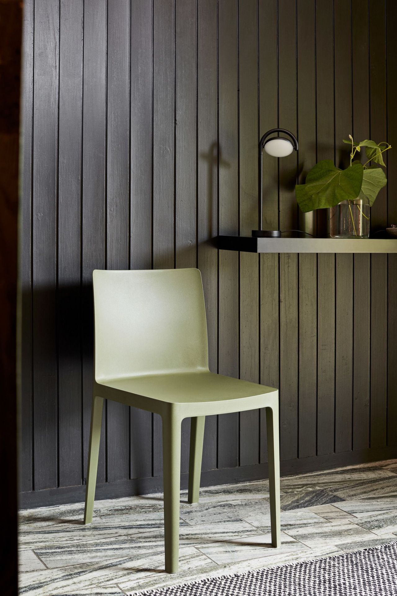Olivefarbener Elementaire Outdoor Stuhl vor dunkler Holzwand, minimalistisches Design für Garten und Terrasse.