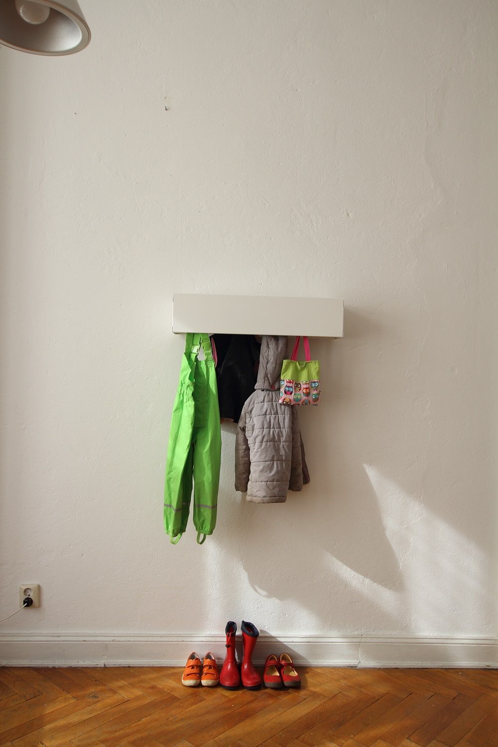Weiße Wandgarderobe CR Linea1 von Müller Möbelwerkstätten mit Kinderkleidung und Schuhen an einer weißen Wand.