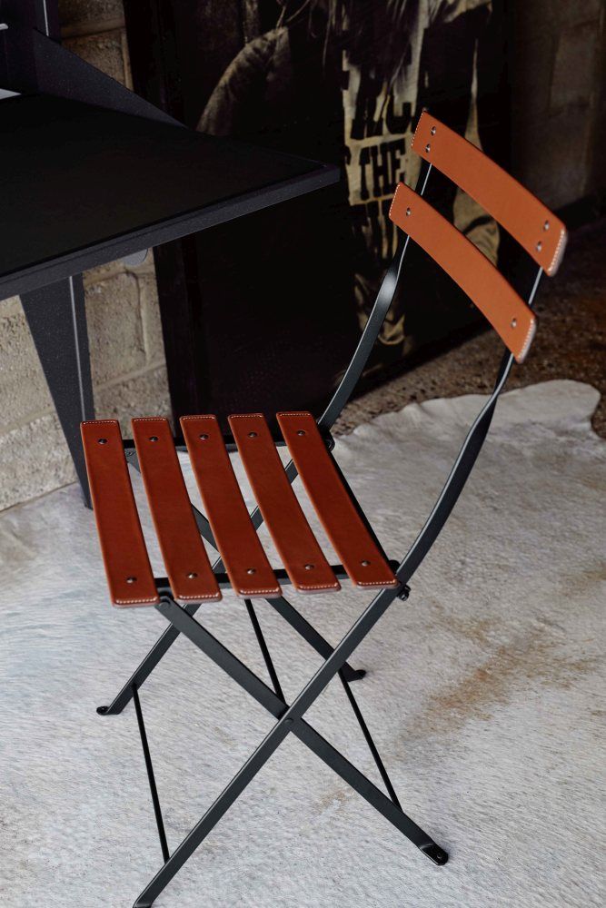 Fermob Bistro Stuhl: Klappbarer Outdoor-Stuhl mit braunen Lederriemen und schwarzem Metallgestell.