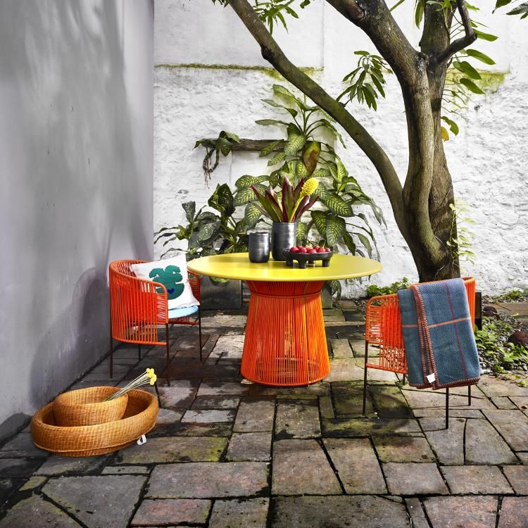 Ames Caribe Esstisch Outdoor, gelbe Tischplatte und orangefarbenes Untergestell, mit Stühlen im Garten.