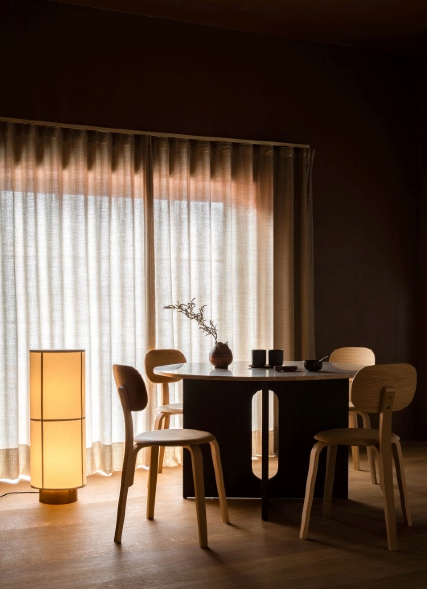 Audo Hashira Stehleuchte im Interieur neben Esstisch und Stühlen, warmes Licht, gemütliche Atmosphäre.
