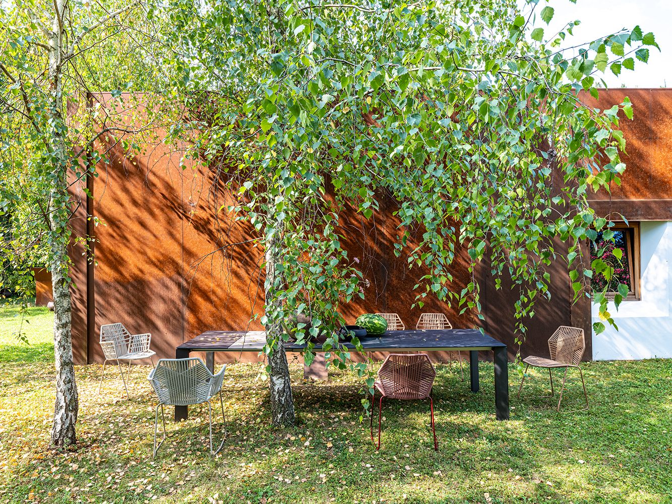 Mehrere Tropicalia Armchair Outdoor Armlehnenstühle von Moroso um einen Tisch im Garten, modernes Outdoor-Mobiliar.