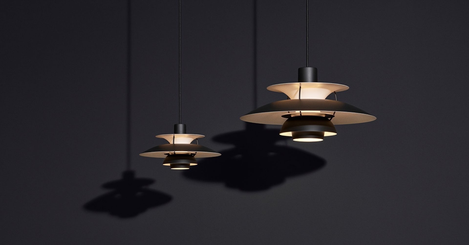 Zwei moderne, schwarze PH 5 Pendelleuchten von Louis Poulsen vor dunklem Hintergrund, Designklassiker für stilvolle Beleuchtung.