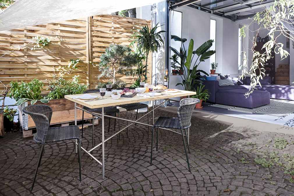 Eiermann Tisch mit heller Tischplatte und Stahlgestell im Garten, gedeckt mit Speisen und Getränken.