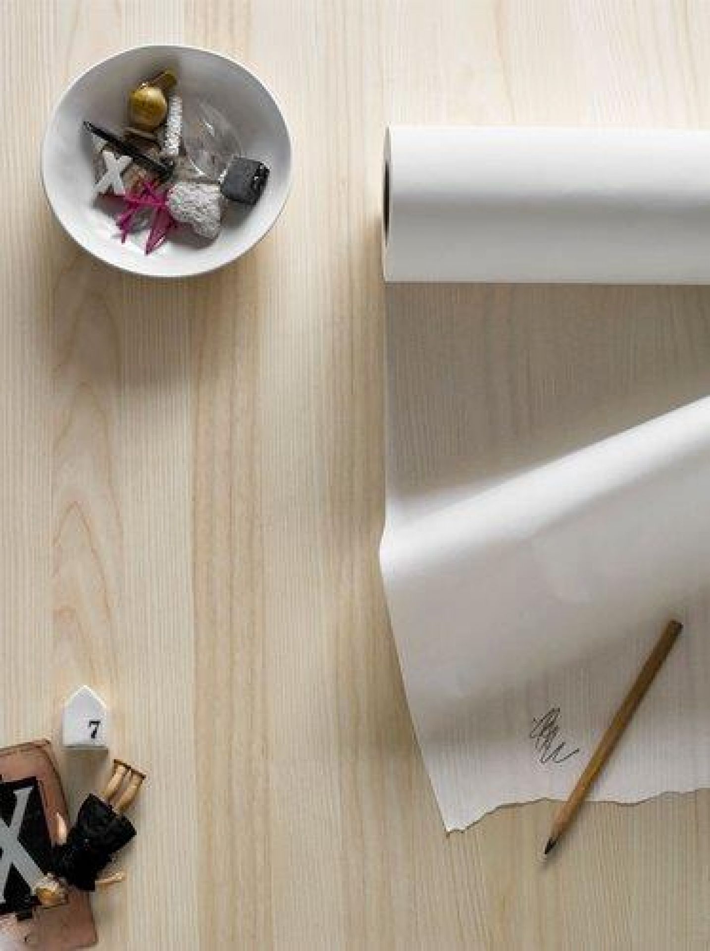 Detailaufnahme eines hellen Fritz Hansen Essay Tisches mit Papierrolle, Stift und dekorativen Accessoires.