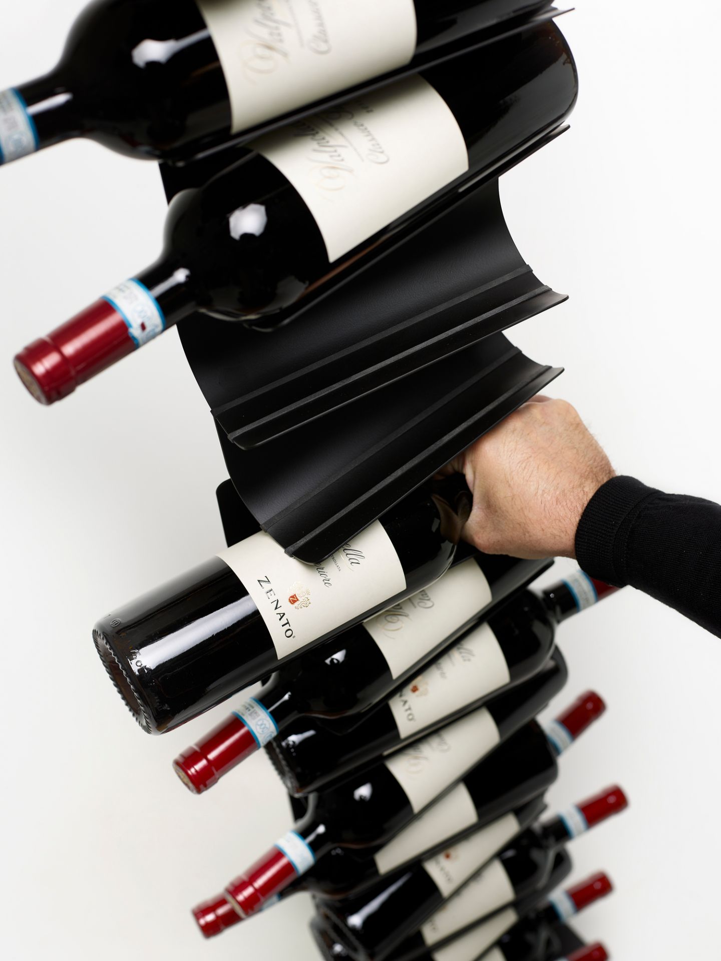Schwarzes Ptolomeo Vino Weinregal von Opinion Ciatti mit Weinflaschen, gehalten von einer Hand.