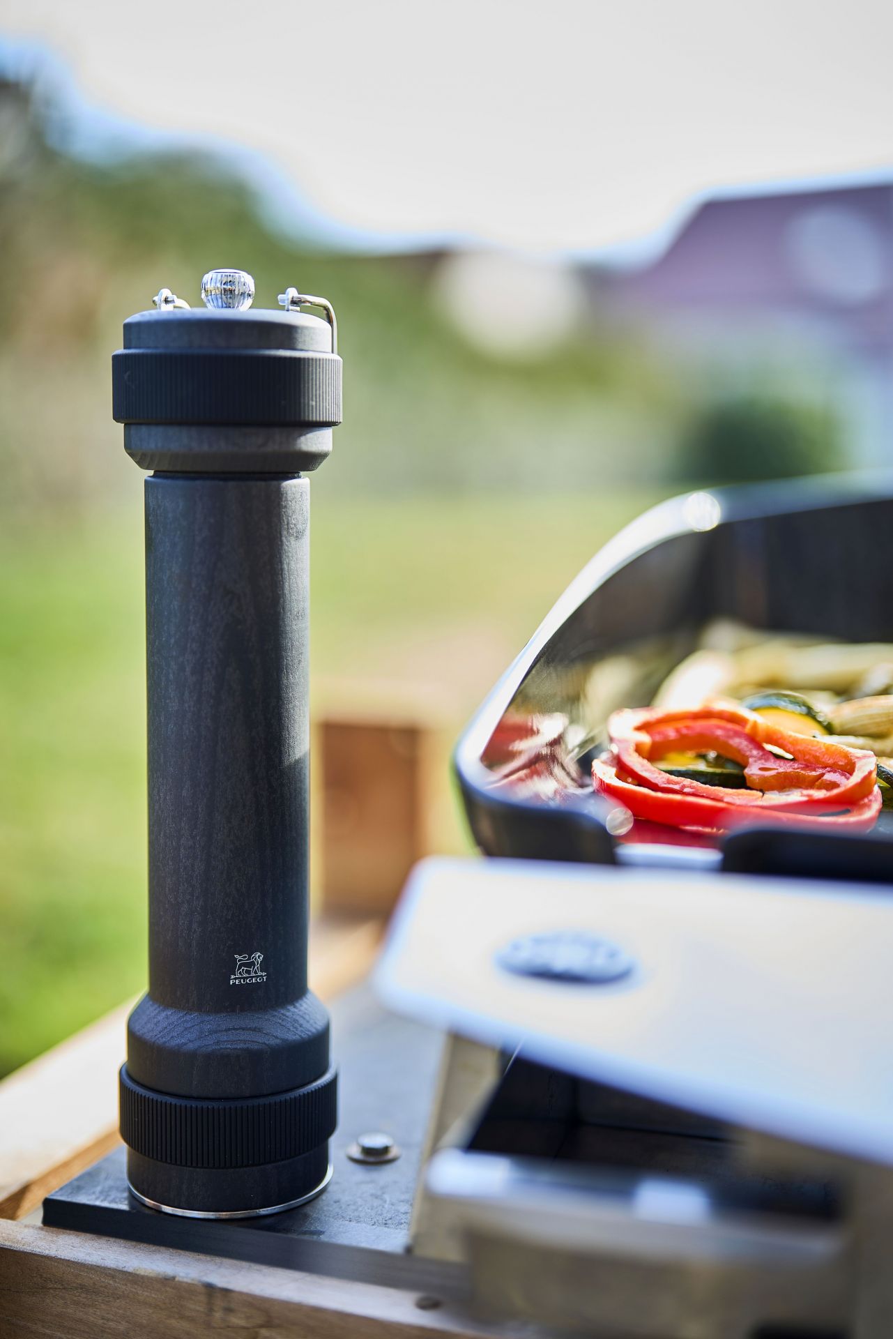 Peugeot BBQ Pfeffermühle graphit 30 cm neben Grill mit Gemüse, ideal für Outdoor-Barbecue.