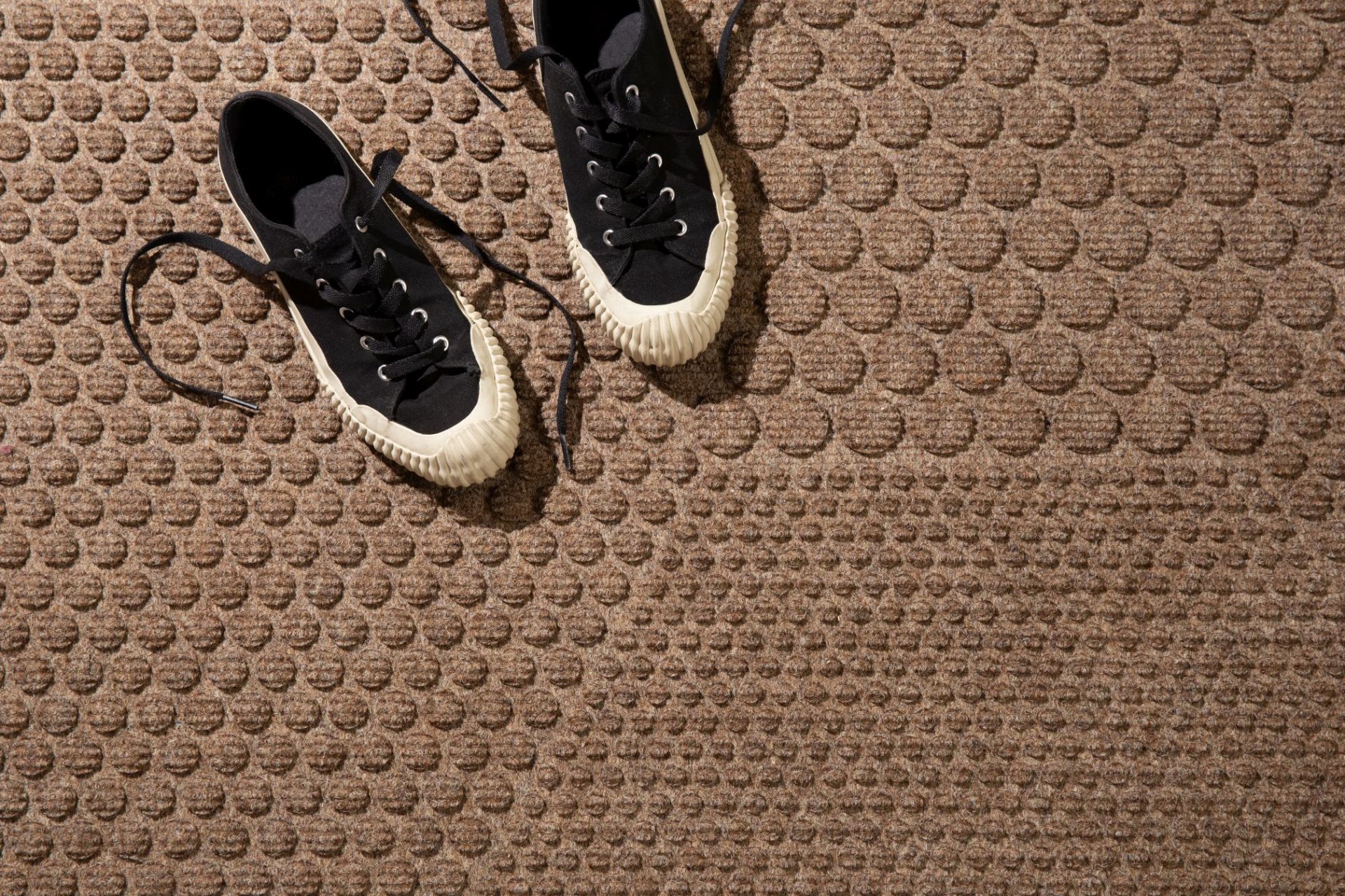 Hex Fußmatte Desert: Detailaufnahme mit zwei schwarzen Sneakern auf der braunen Fußmatte.