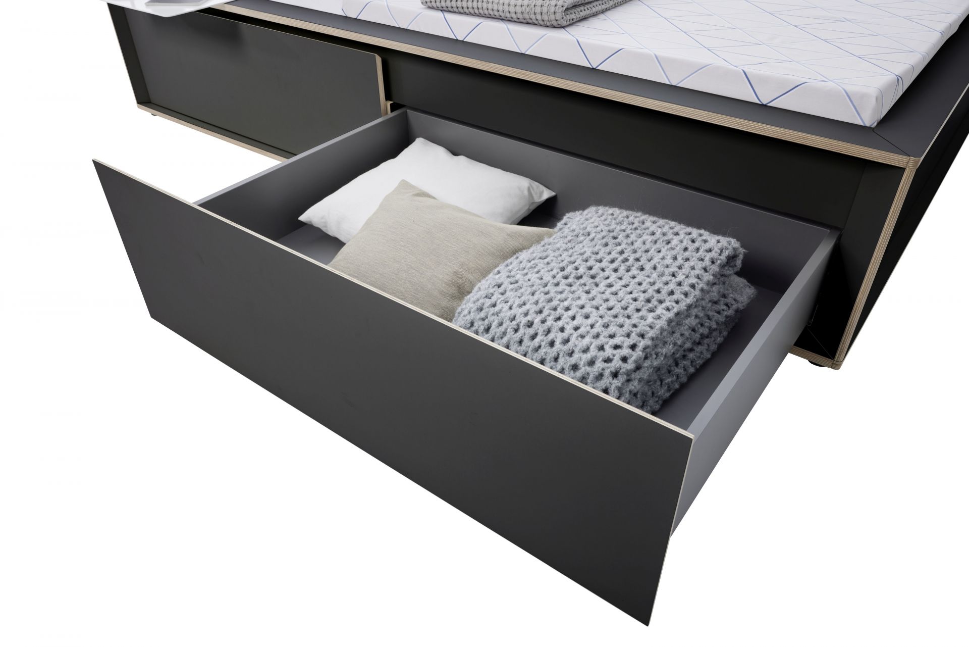 Spaze Bett von Müller Möbelwerkstätten mit offener Schublade, Kissen und grauer Strickdecke.