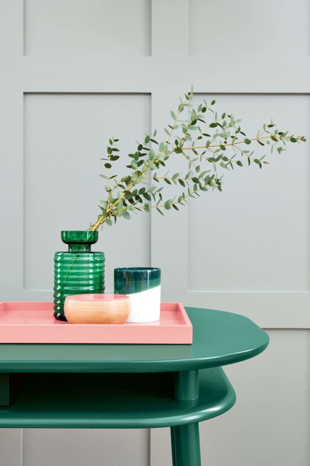 Schreibtisch Schönbuch: Moderner, grüner Beistelltisch mit Deko-Elementen wie Vase, Schale und Tablett vor grauer Wand.