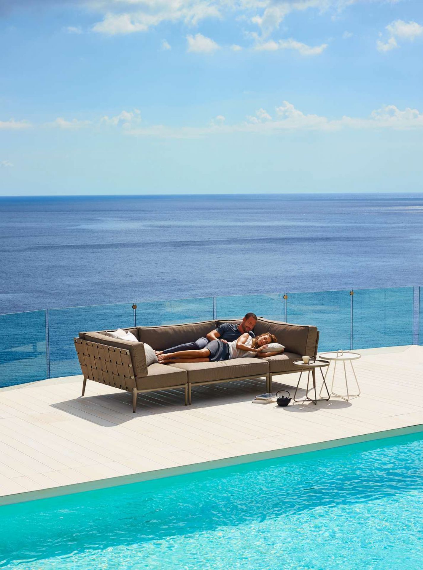 Conic Outdoor Sofa: Paar entspannt auf grauem Cane-Line 2-Sitzer Modulsofa am Pool.