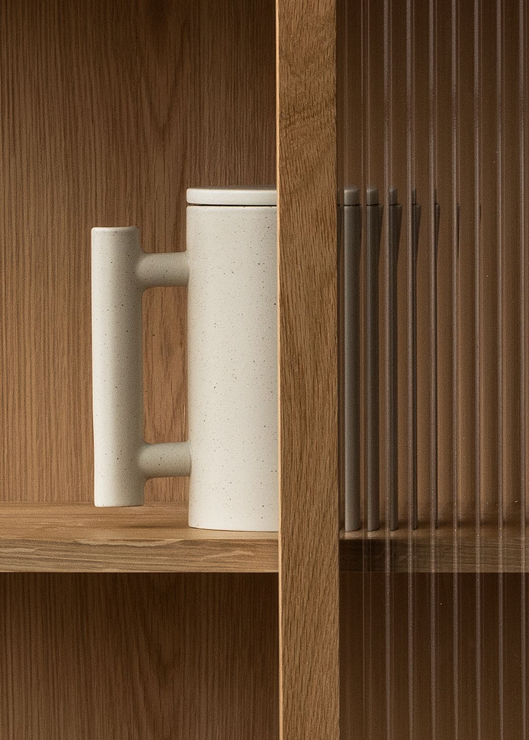 Detailaufnahme des Audo Copenhagen Curiosity Cabinet Schranks mit Keramikkanne und geriffeltem Glas.