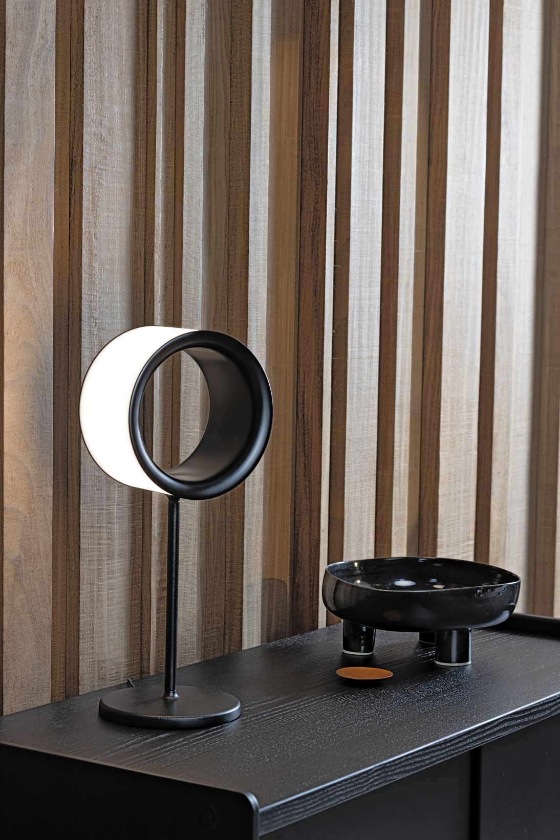 Lost Tischleuchte von Magis, moderne LED-Lampe mit kreisförmigem Design auf einem schwarzen Nachttisch.