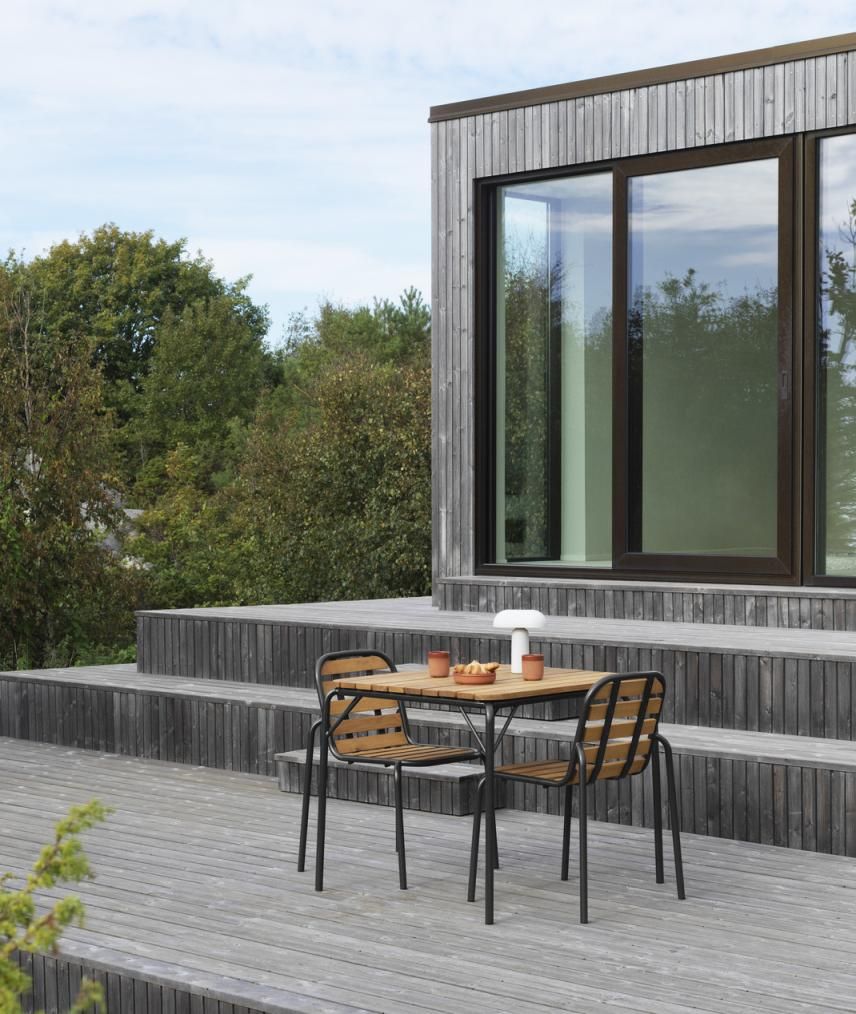 Normann Copenhagen Vig Chair Wood Stuhl Outdoor mit Tisch auf Holzterrasse vor modernem Haus.