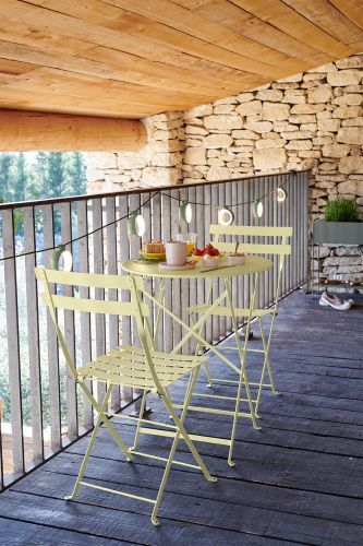 Gelber Fermob Bistro Tisch mit zwei Stühlen auf einem Balkon mit Frühstücksgedecken. Outdoor Möbel.